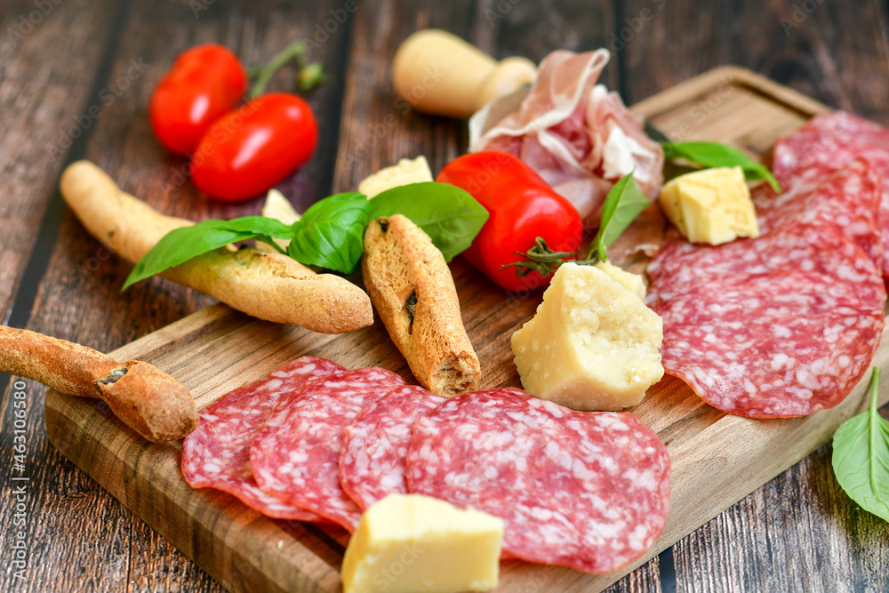Italian dried thinly sliced artisan pork salami Milano , parmesan cheese, tomatoes and fresh basil on wooden background .Rustic home made italian snack. Italian dried thinly sliced artisan pork salami Milano , parmesan cheese, tomatoes and fresh basil on wooden background .Rustic home made italian snack.