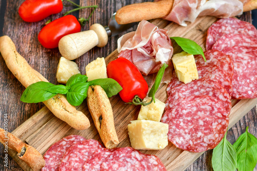 Italian dried thinly sliced artisan pork salami Milano , parmesan cheese, tomatoes and fresh basil on wooden background .Rustic home made italian snack.