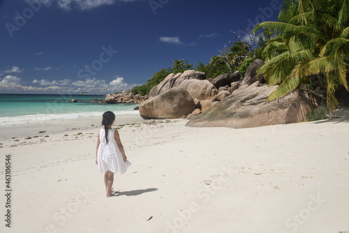 Girl in white dress walking on tropical beach near indian ocean at Syechelles island of Praslin