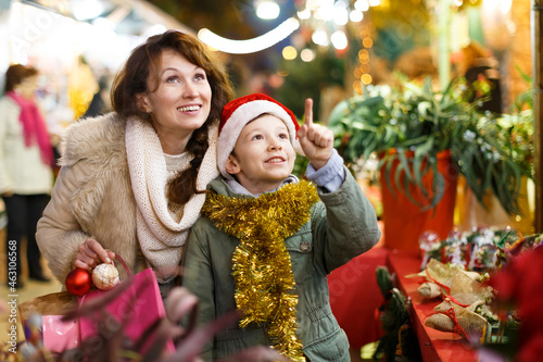 Young family of mother and son shopping Christmas decorations on market pointing to something