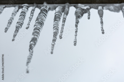 Dangerous icicles hanging from the roof against cloudy sky background