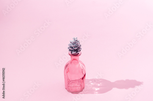 A beautiful pink perfume bottle with a silver pine cone instead of a cork. Christmas or New year celebration gift. Festive end of the year creative concept.