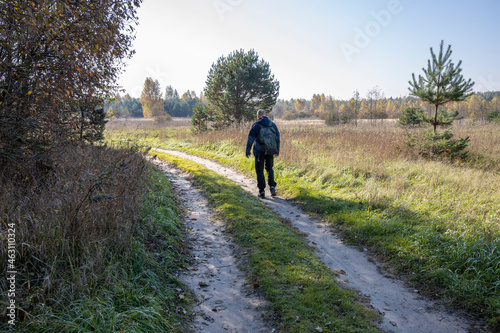 A tourist walks along a country road early in the morning. A man with a backpack on the background of a field illuminated by sunlight.