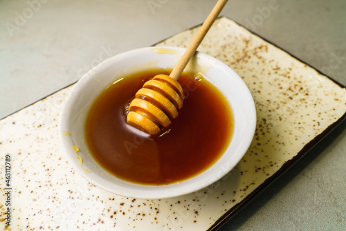 Fresh dark honey in white ceramic bowl with wooden honey spoon