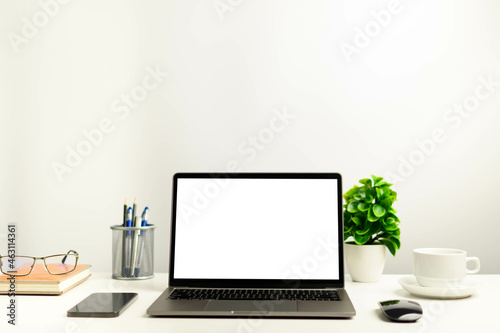 A working concept using technology, notebook, smartphones, devices. Blank white screen laptop on a white table in the office. Copy space on upper for design or text, Closeup, Gray, and blur background