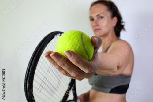 white woman prepares to serve in tennis. tennis ball and racket in the foreground. © Elena