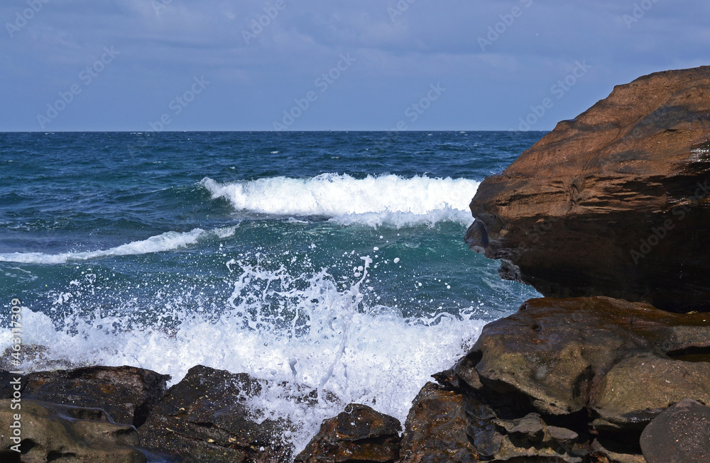 View from the rocky coast to the sea with splashes and white sea foam