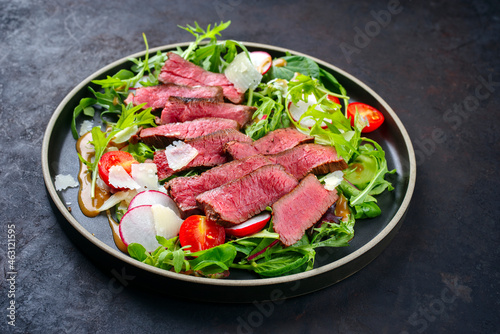 Modern style traditional fried dry aged bison beef rump steak slices with vegetable, lettuce and mustard dressing served as close-up on a Nordic design plate with copy space