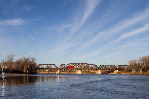 Train crossing a bridge over a body of water with blue skies and soft clouds in the background, Winnipeg, Manitoba