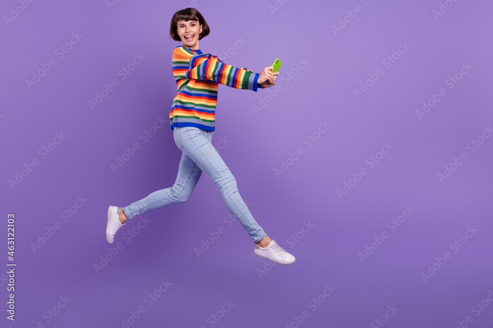 Photo of energetic influencer lady jump hold phone wear striped sweater jeans shoes isolated purple color background