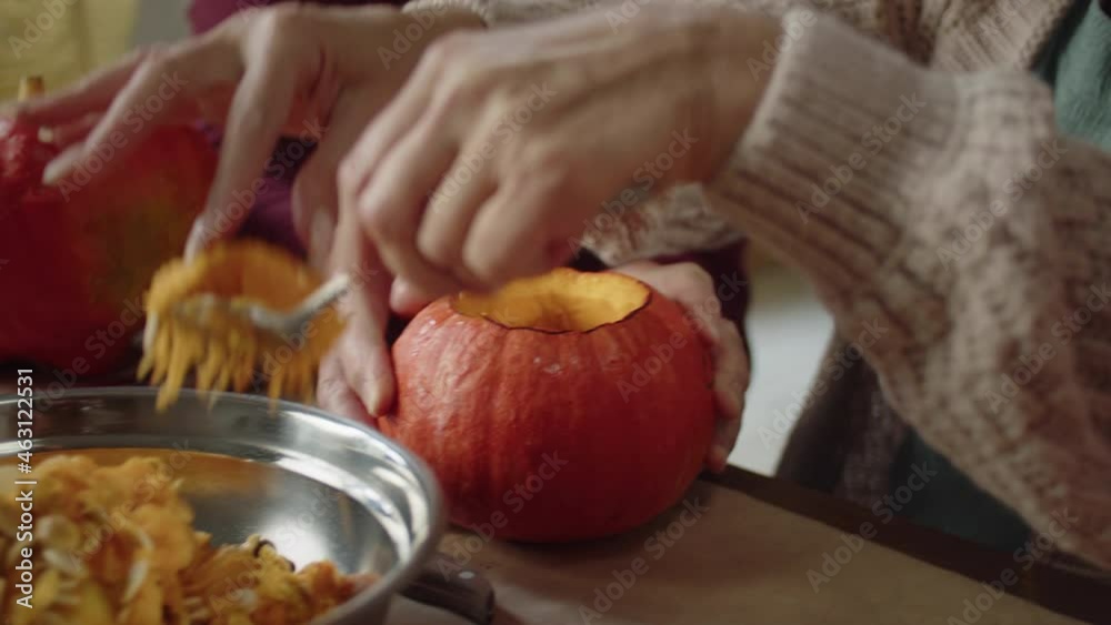 A woman with a spoon takes out the pulp from the pumpkin and puts it in a metal misk A woman with a spoon takes out the pulp from the pumpkin and puts it in a metal misk