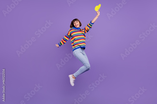 Photo of crazy romantic lady jump hold yellow heart wear striped sweater jeans shoes isolated purple color background