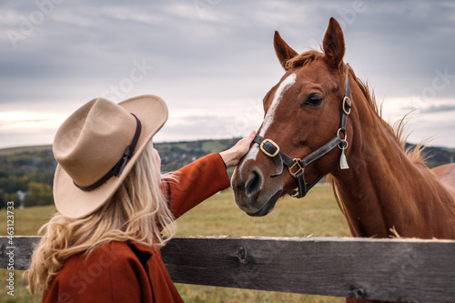 Woman with cowboy hat with her thoroughbred horse at ranch. Cowgirl in animal farm. Friendship between people and horse