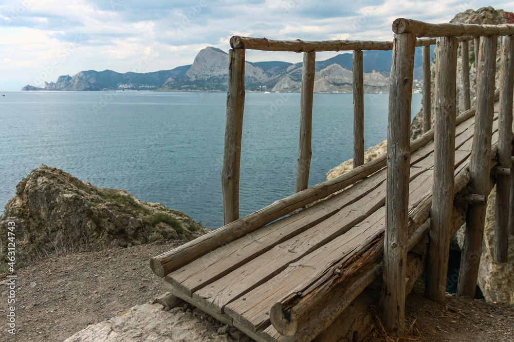 A path along the sea with a wooden bridge. The wooden bridge against the background of the blue sea and mountains