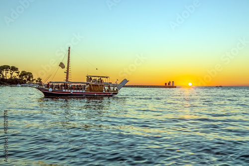 Image of a sunset from the harbor of the Croatian coastal town of Porec with a passing tourist boat