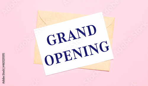 On a light pink background - a craft envelope. It has a white sheet of paper that says GRAND OPENING