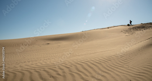 Unrecognized person walking in sand dunes dry land in midday
