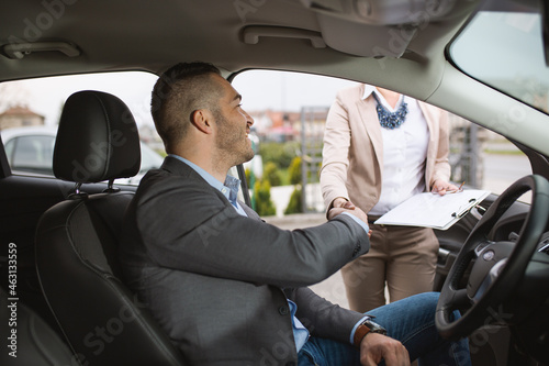 A young businessman anjoys buying a new car.He talks to a sales agent at a car dealership.