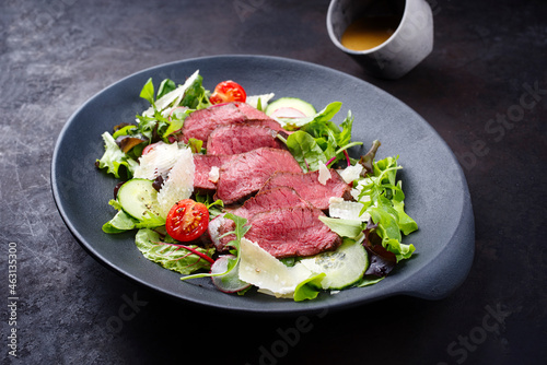 Modern style traditional fried dry aged bison beef rump steak slices with vegetable, lettuce and mustard dressing served as top view on a Nordic design plate