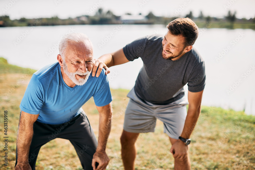 Athletic senior man takes break while running with his adult son by in nature. Athletic senior man takes break while running with his adult son by in nature.
