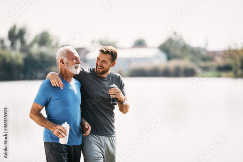 Fototapeta Naklejka Na Ścianę i Meble -  Happy athletic man and his father talk and drink water after running in nature. Copy space.