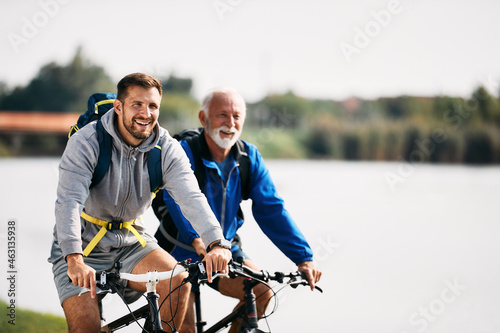 Happy athletic man enjoys in cycling with his senior father by the river. Copy space. photo