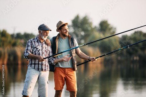 Happy mature man and his adult son enjoy while river fishing together.