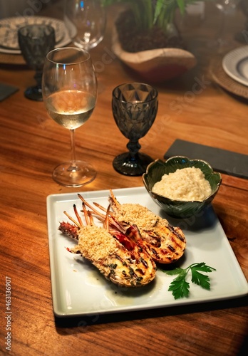 lobster cut into two parts, decorated with green vegetables on the plate and wine
