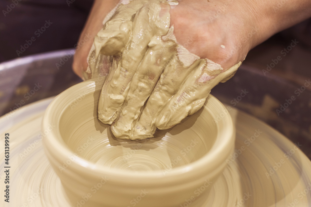 Closeup view of female ceramics artist hands shapes clay on pottery wheel. Artist workshop.