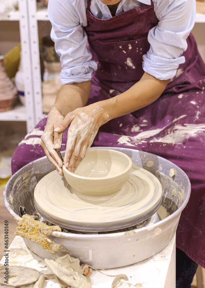 Woman ceramic artist molding clay on pottery wheel at art workshop. Mid section view.