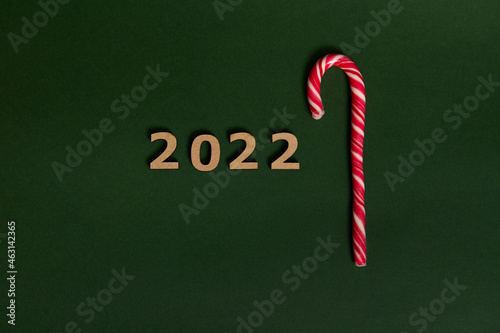 Conceptual tudio shot of wooden numerals 2022 and sugary striped white and red Christmas lollipop, sweet candy cane, symbolizing New year and Christmas traditional event with space for advertisement photo