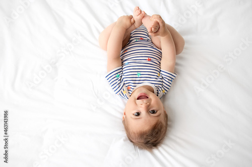 Top view of cute baby lying on white bed holding his feet