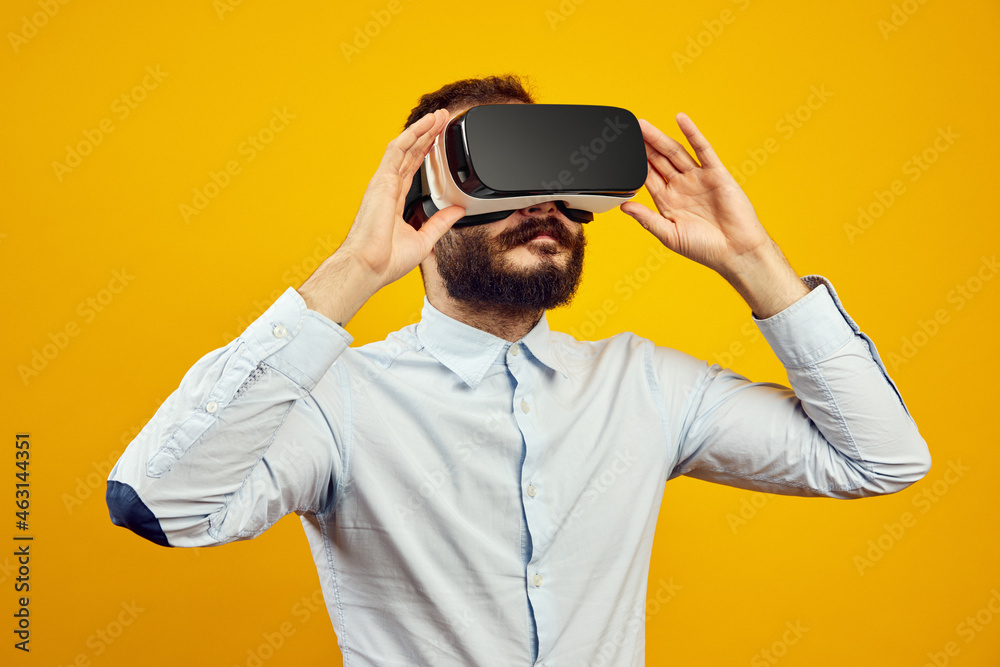 Young bearded man smiling wide while wearing VR headset on yellow background Young bearded man smiling wide while wearing VR headset on yellow background