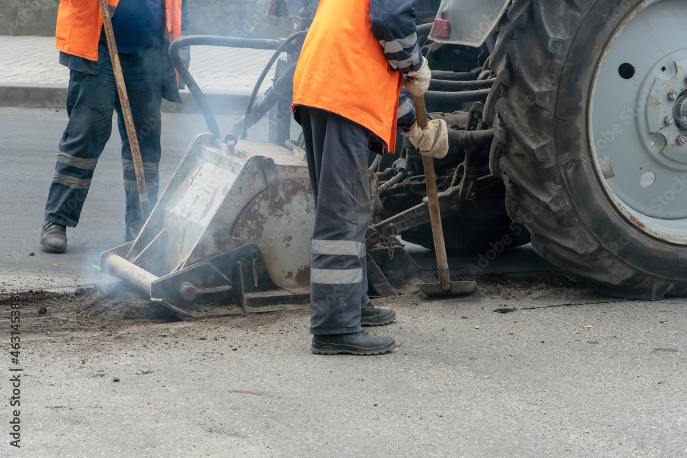 asphalt repair in the city. A team of workers in special clothes stands next to a tractor and asphalt laying equipment. asphalt repair in the city. A team of workers in special clothes stands next to a tractor and asphalt laying equipment.