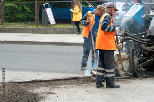 asphalt repair in the city. A team of workers in special clothes stands next to a tractor and asphalt laying equipment.