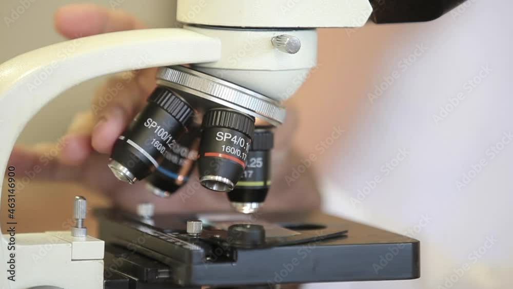 Mãos de cientista com close-up de microscópio filmado em laboratório
