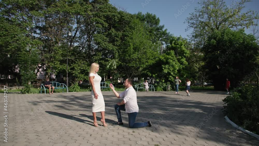 marry me, romantic man kneels with ring in box in his hands and proposes to charming woman in park background of trees