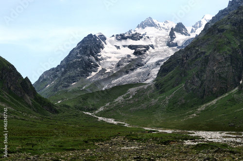 Snowy peak and green blooming valley with a river