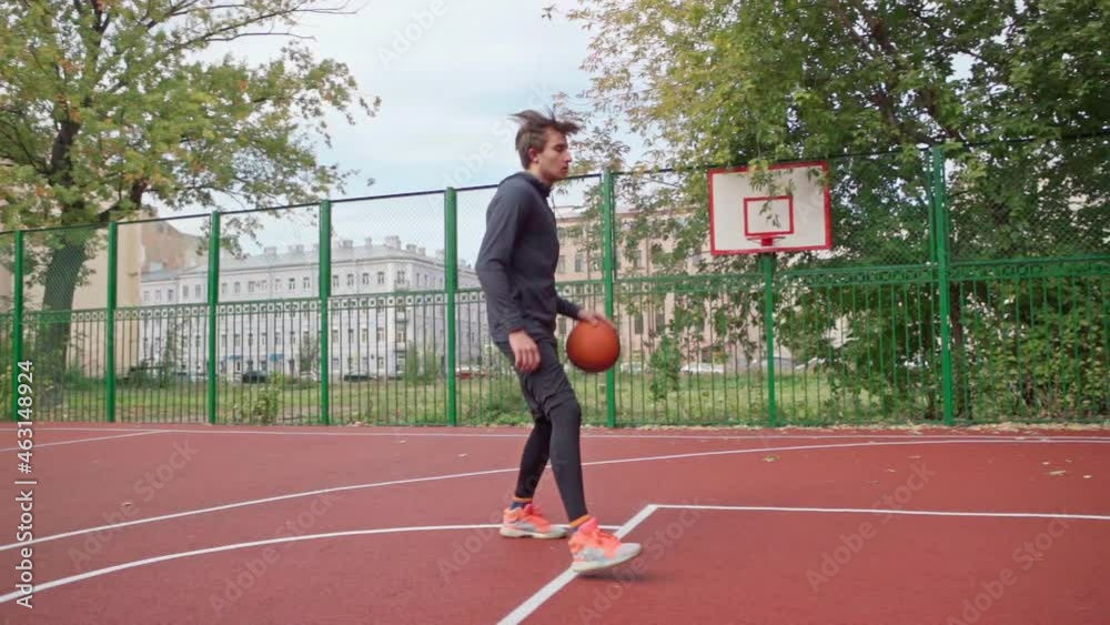 Tracking side view slow motion shot of teenage boy handling ball and throwing into hoop scoring goal. Skilled young man practicing basketball on outdoor college court Tracking side view slow motion shot of teenage boy handling ball and throwing into hoop scoring goal. Skilled young man practicing basketball on outdoor college court