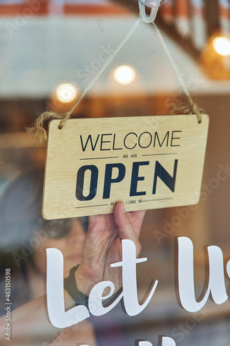 Unrecognizable person turning open signboard on door of cafe