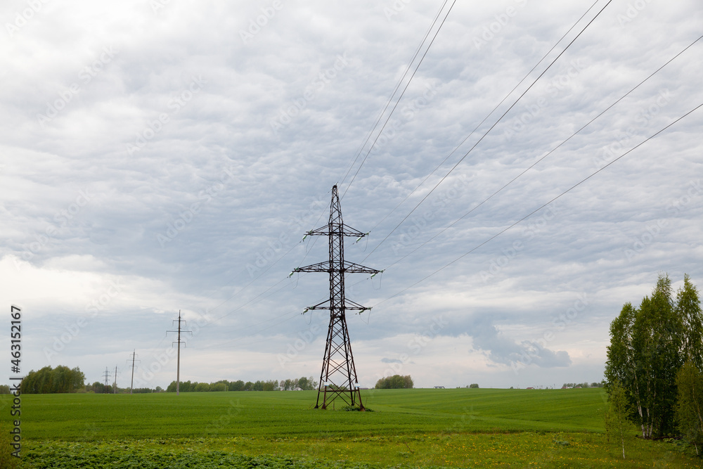 High voltage lines and power pylons in a flat and green agricultural landscape on a sunny day with cirrus clouds in the blue sky.