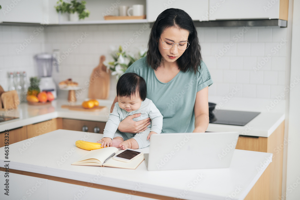 Young mother with baby using laptop at table in morning Young mother with baby using laptop at table in morning