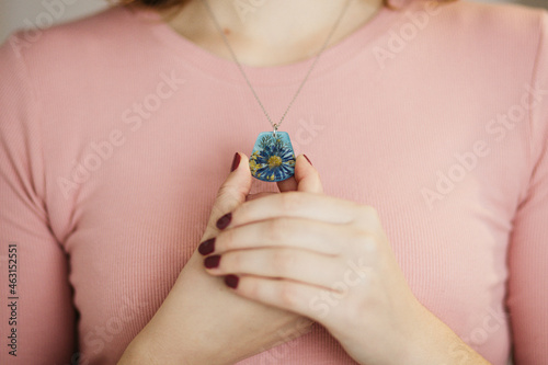 Close up of female hands holding floral epoxy necklace photo