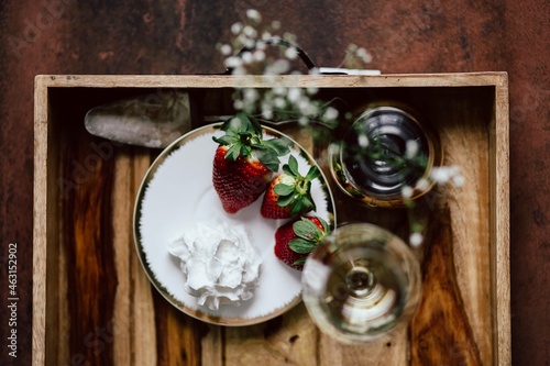 Strawberries with cream and glass of white wine on wooden tray