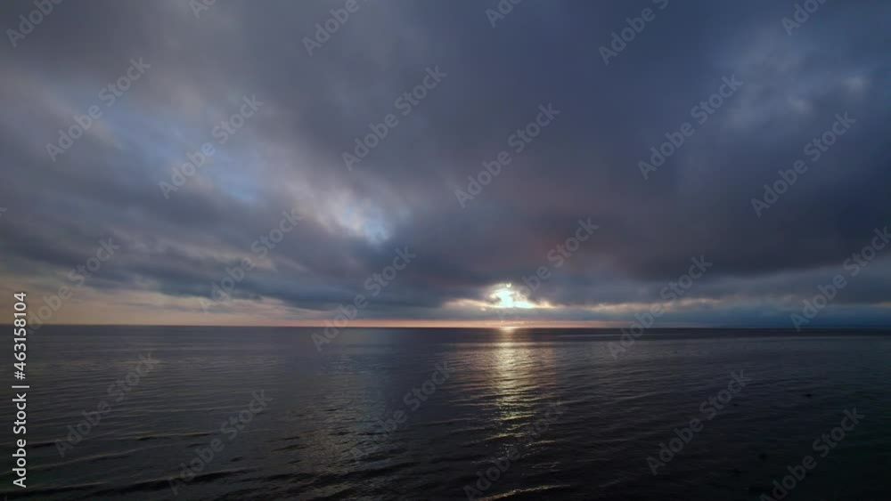 Aerial flight over the sea with powerful clouds at sunset. The sun appears disc from behind the clouds and hides again.  the sun's rays pass through the clouds and are reflected in the sea.
