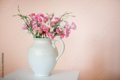 Bouquet with eustoma  summer flowers in a white vase  on a pink-beige background.