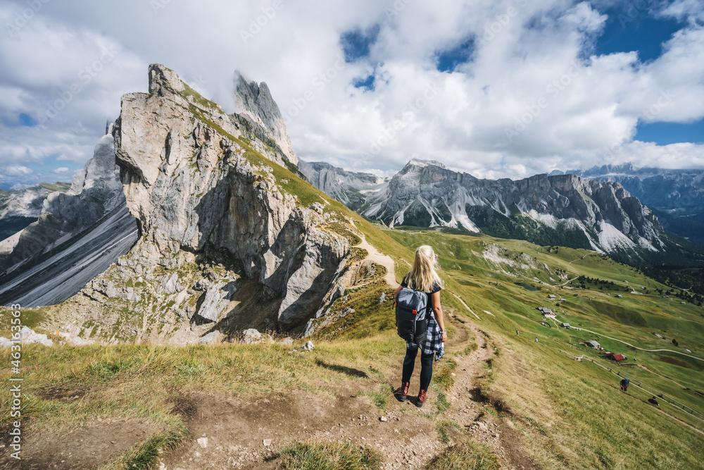 Women hiker on hiking trail path and epic landscape of Seceda peak in Dolomites Alps, Odle mountain range, South Tyrol, Italy, Europe