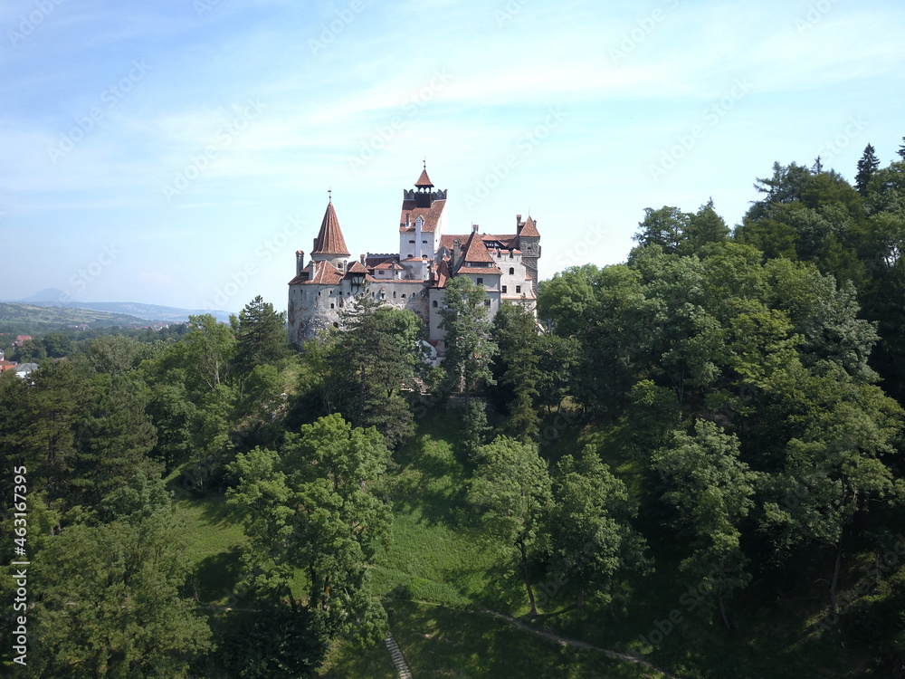 Aerial view of Bran castle in Transylvania, Romania with white walls, red roofs, green trees and blue sky