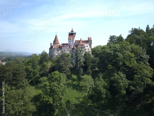 Aerial view of Bran castle in Transylvania, Romania with white walls, red roofs, green trees and blue sky © Andreas