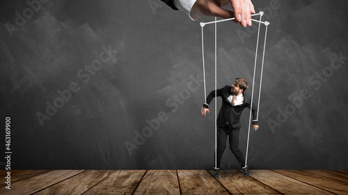 Fotografia businessman hanging on strings like a puppet from a hand in front of a blackboar
